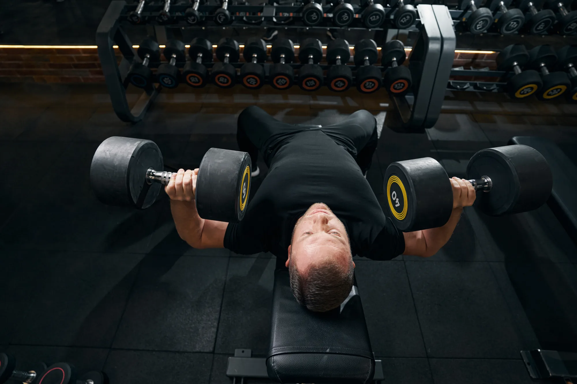 Athletic male lifting hand weights on workout bench