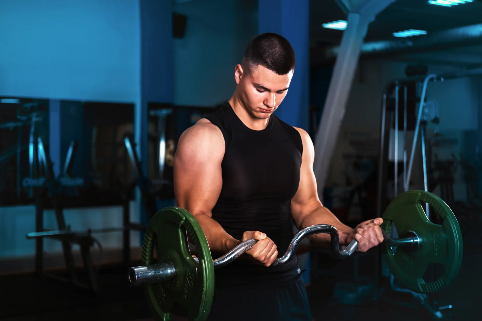A young athlete does exercises for biceps, a barbell with a curved bar. The man in the gym.