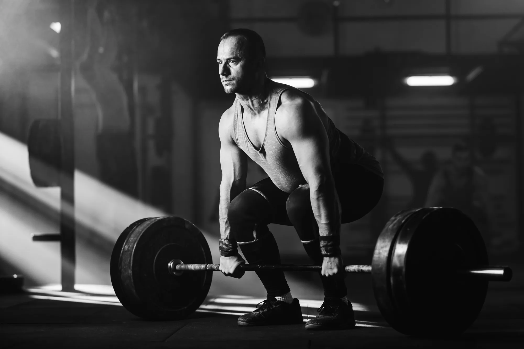 Black and white photo of athletic man exercising deadlift with barbell.