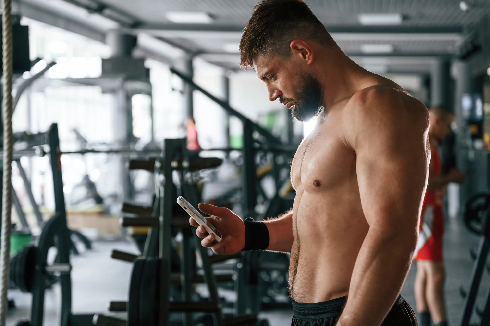 Muscular man taking a break in the gym with a smartphone