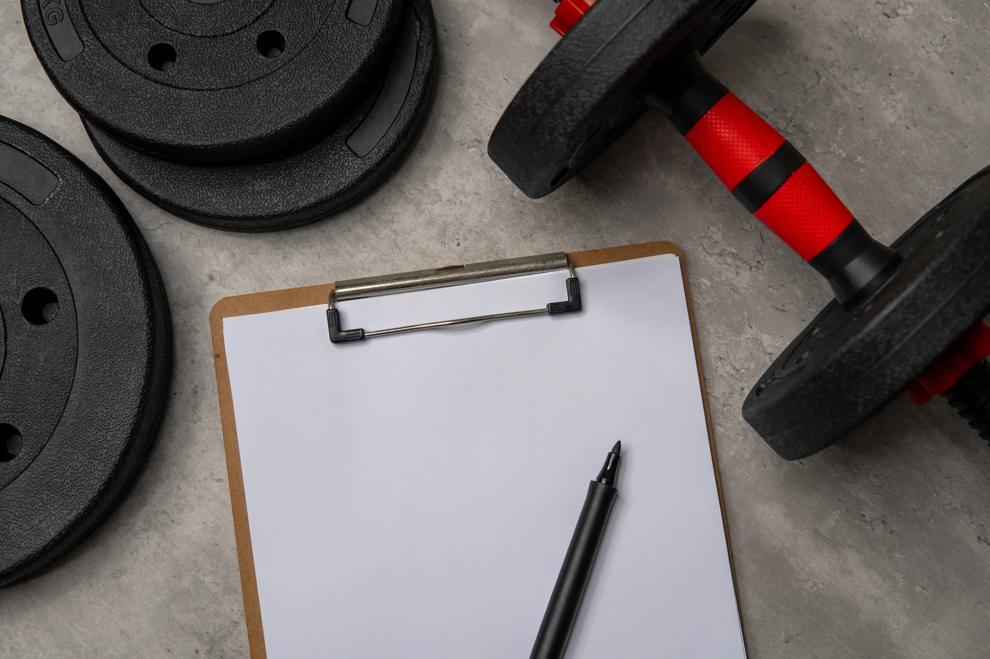 A blank white sheet of paper on a clipboard, weight plates and dumbbell.