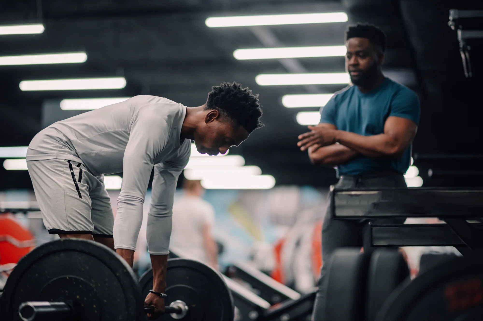 Entschlossene junge trainierende Person, die im Fitnessstudio gemeinsam mit einem Personal Trainer Gewichte hebt.
