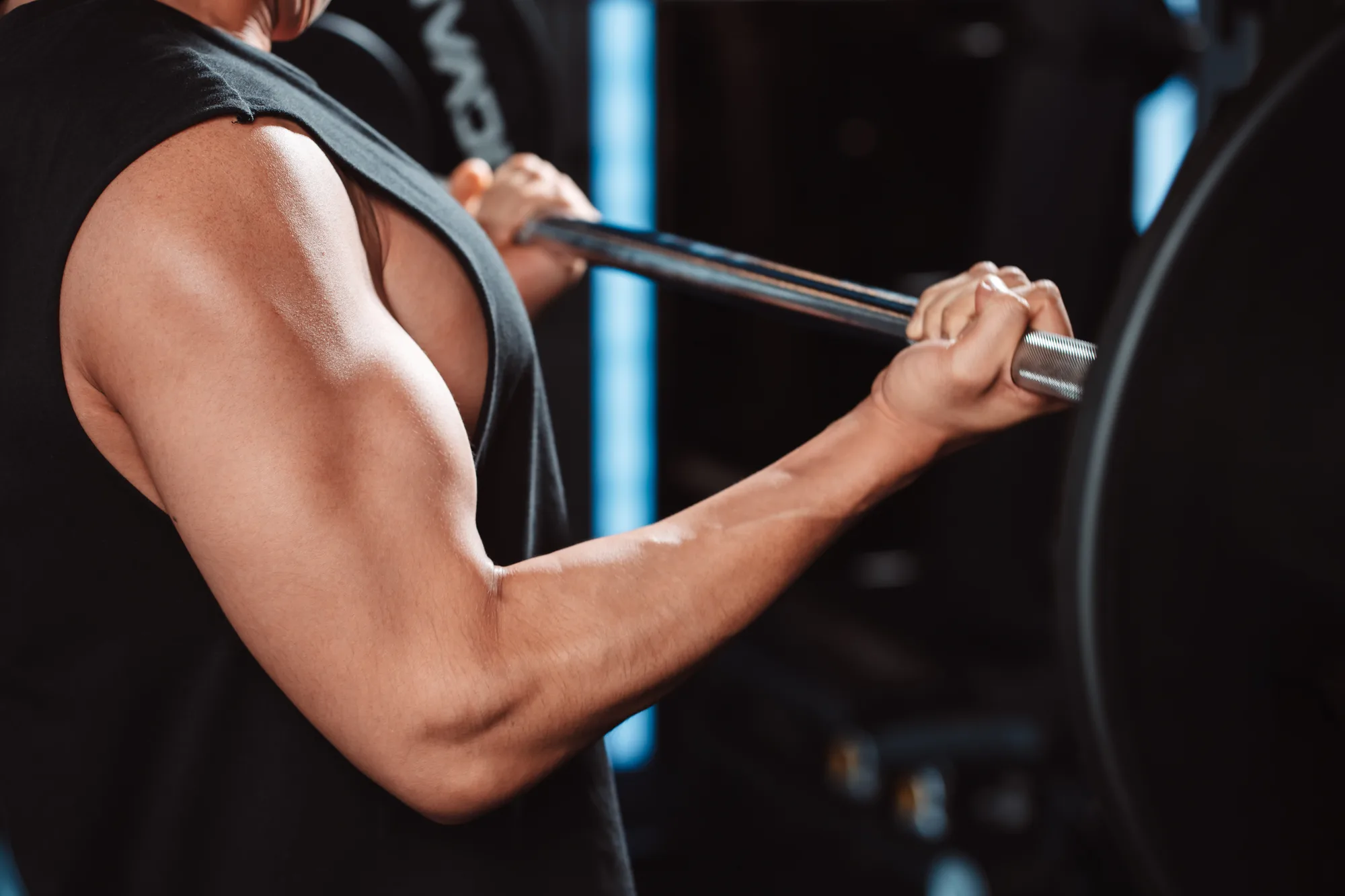 Nahaufnahme des Arms eines Trainierenden mitten in einem Langhantel-Curl im Fitnessstudio.