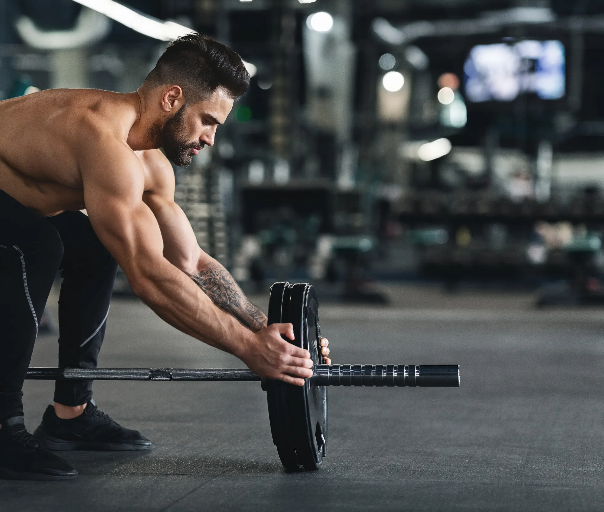 Muscular man changing weights of barbell, empty space